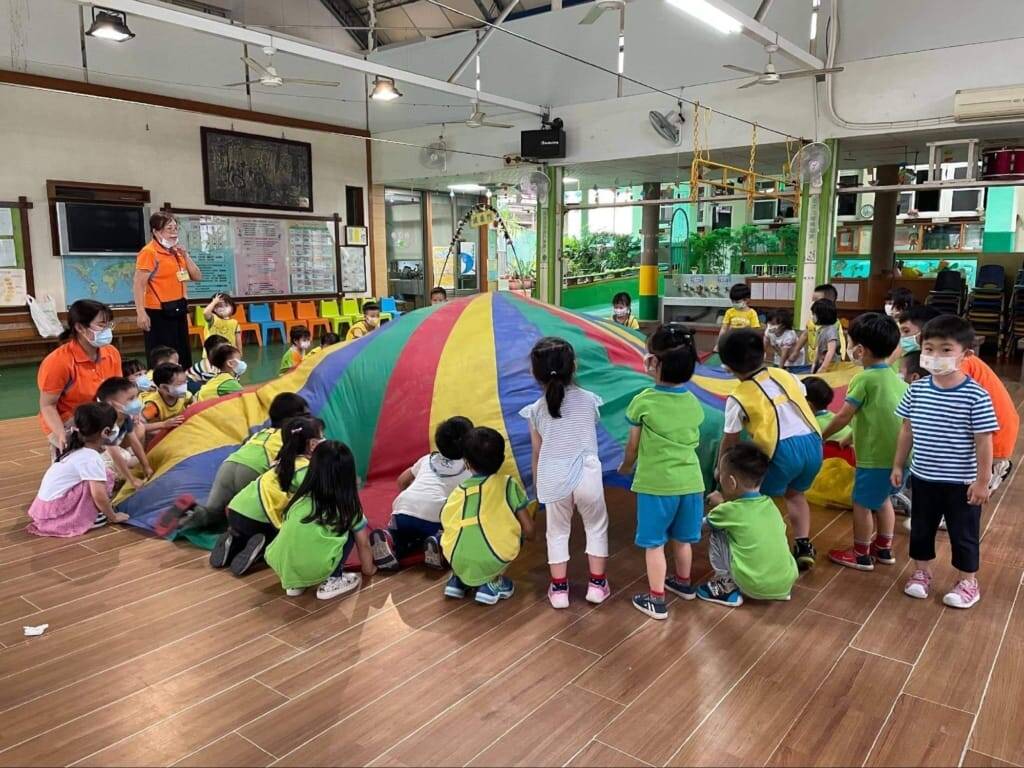 幼兒共同進行氣球傘遊戲，老師在旁協助團體操作