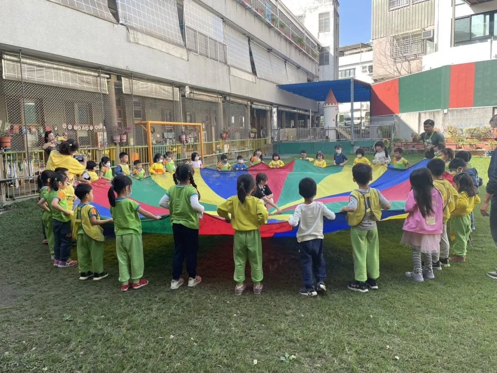 幼兒在戶外共同操作氣球傘進行團體遊戲